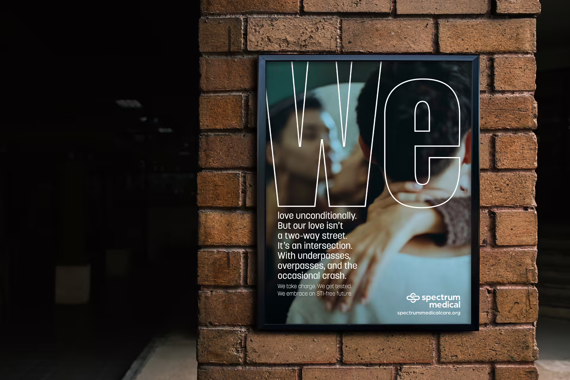 A poster of two people in a frame on a concrete wall in a shaded public area.